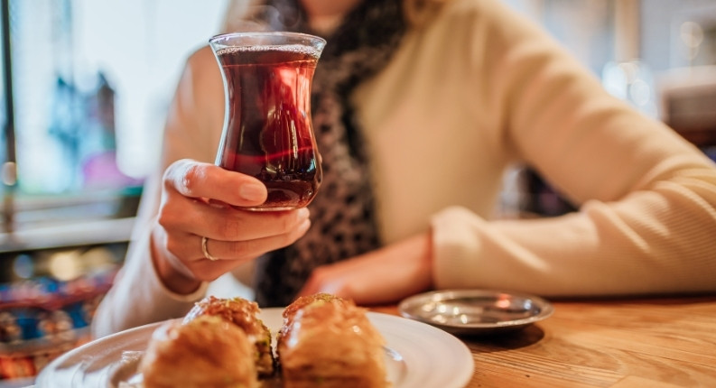Woman holding a glass of traditional Turkish tea with baklava in a cozy café setting