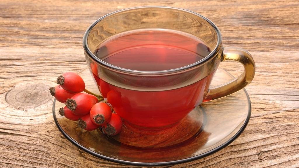 Rosehip tea, vivid ruby red in a glass cup, dried rosehips scattered around it.