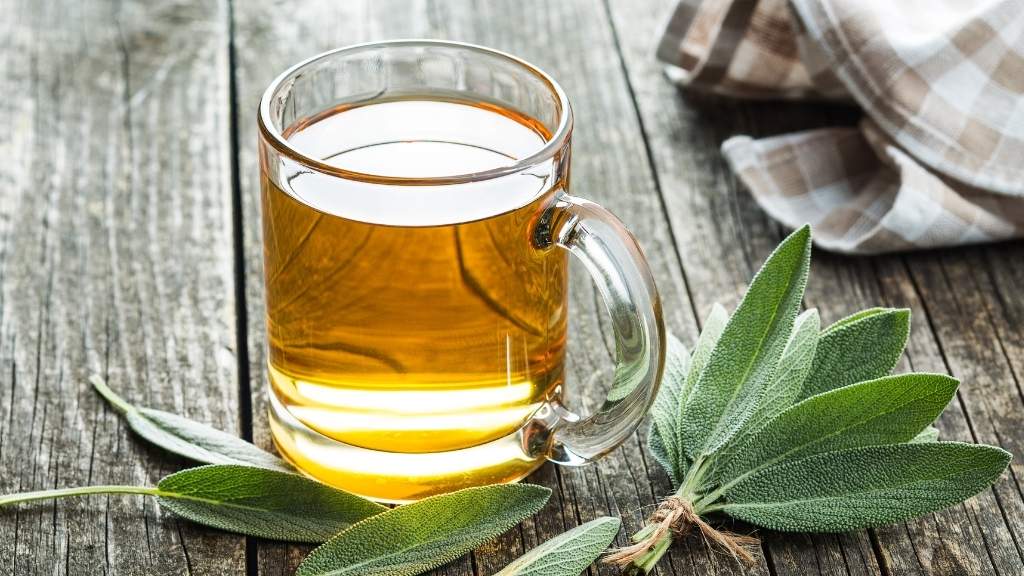 Sage tea (Adaçayı) in a clear glass, green sage leaves beside on wooden table.