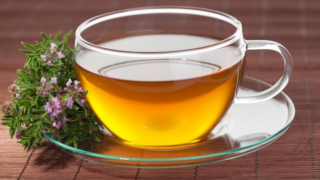 Thyme tea (Kekik) in a clear glass, fresh sage leaves beside on wooden table.